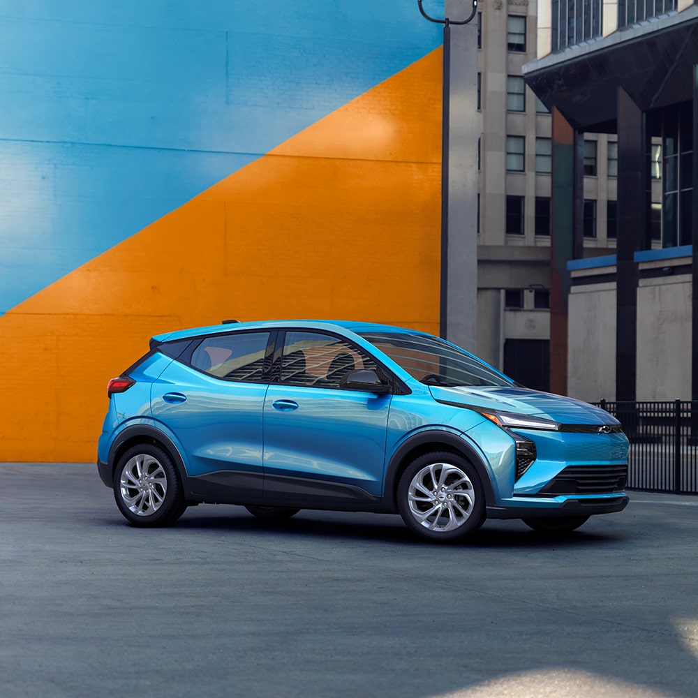 2027 Chevrolet Bolt in Marina Blue Metallic Parked in Front of a Blue and Orange Wall.