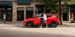 The Side View of a Red 2027 Chevrolet Bolt, with a Man Getting into the Driver's Side Door on a City Street.