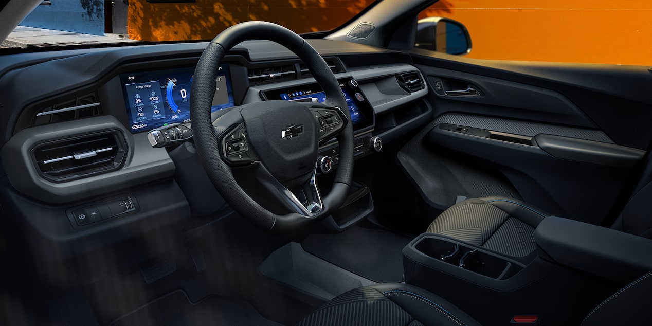 The Interior of a 2027 Chevrolet Bolt EUV, Showing a Dual-Screen Digital Instrument Cluster and Infotainment System with a Black and Gray Leather-Trimmed Steering Wheel and Matching Seats.