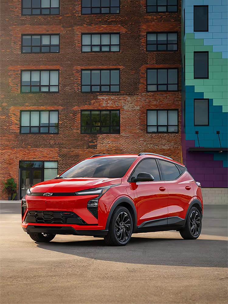 A Habanero 2027 Chevrolet Bolt is Parked in Front of A Brown Brick Building.
