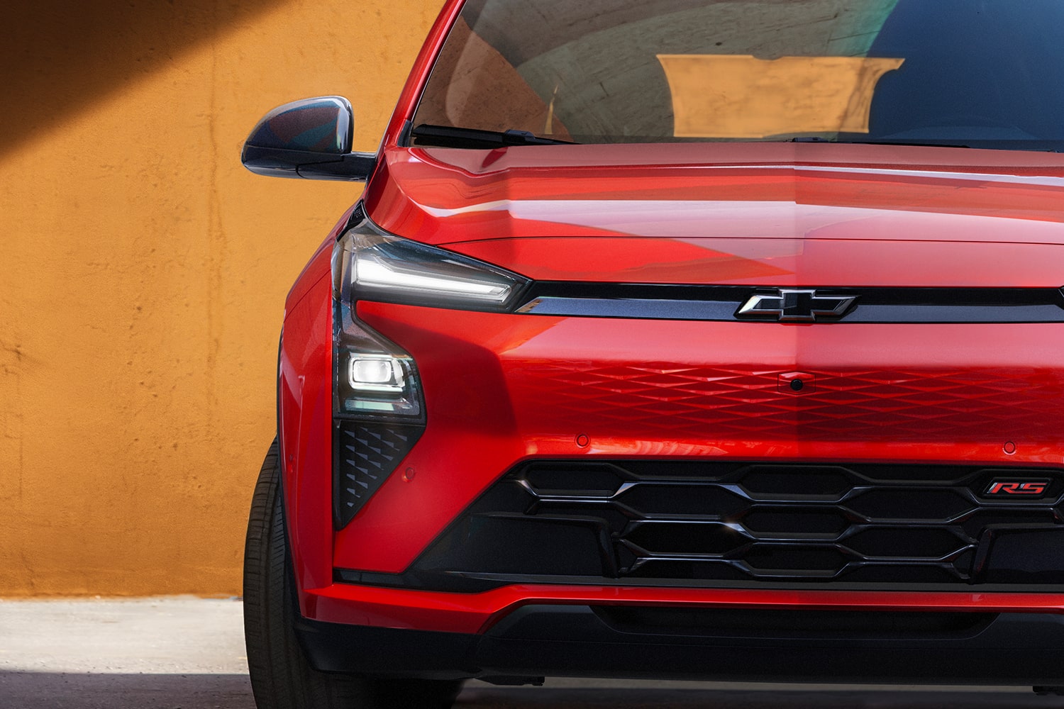 A Close-Up of the Front of a Habanero 2027 Chevrolet Bolt RS, Showing the Headlights, Black Grille, and the RS Badge.