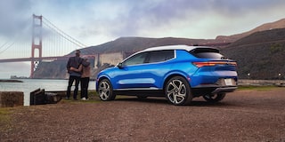 Vista trasera de perfil de Equinox EV Azul estacionada mientras una pareja mira hacia el puente Golden Gate
