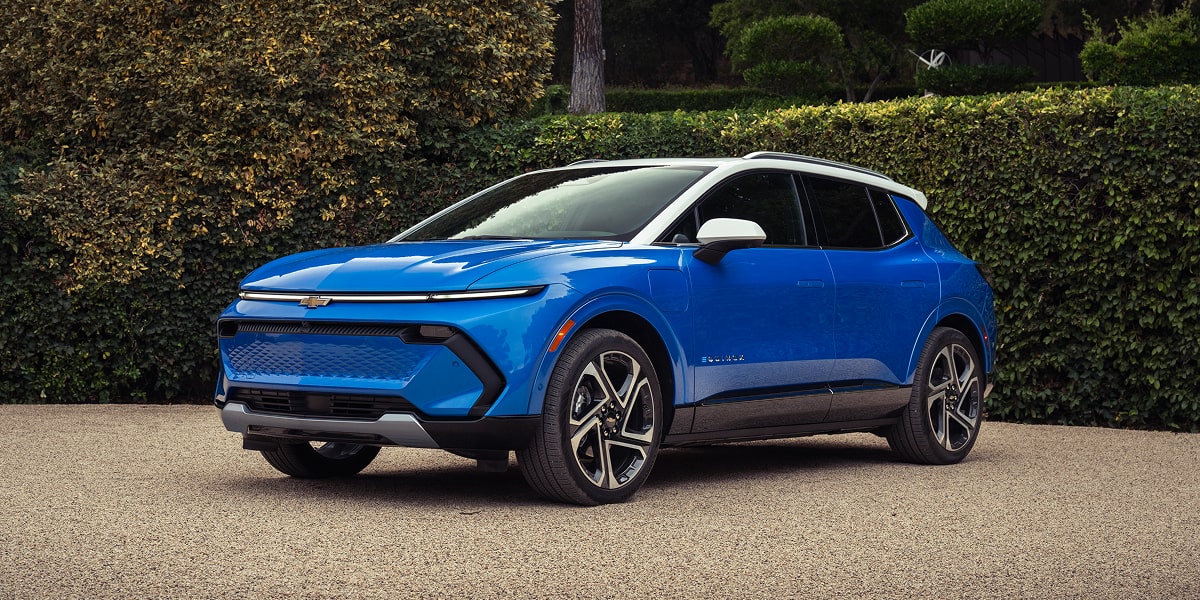 Front Side View of a Blue Equinox EV Parked on a Gravel Driveway With Hedges