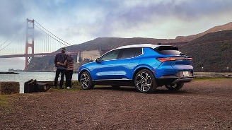 Vista trasera de perfil de Equinox EV Azul estacionada mientras una pareja mira hacia el puente Golden Gate