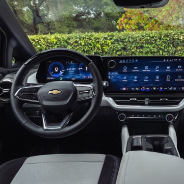 Vista interior del asiento del conductor de Chevy Equinox EV con vista a un lago bordeado de árboles