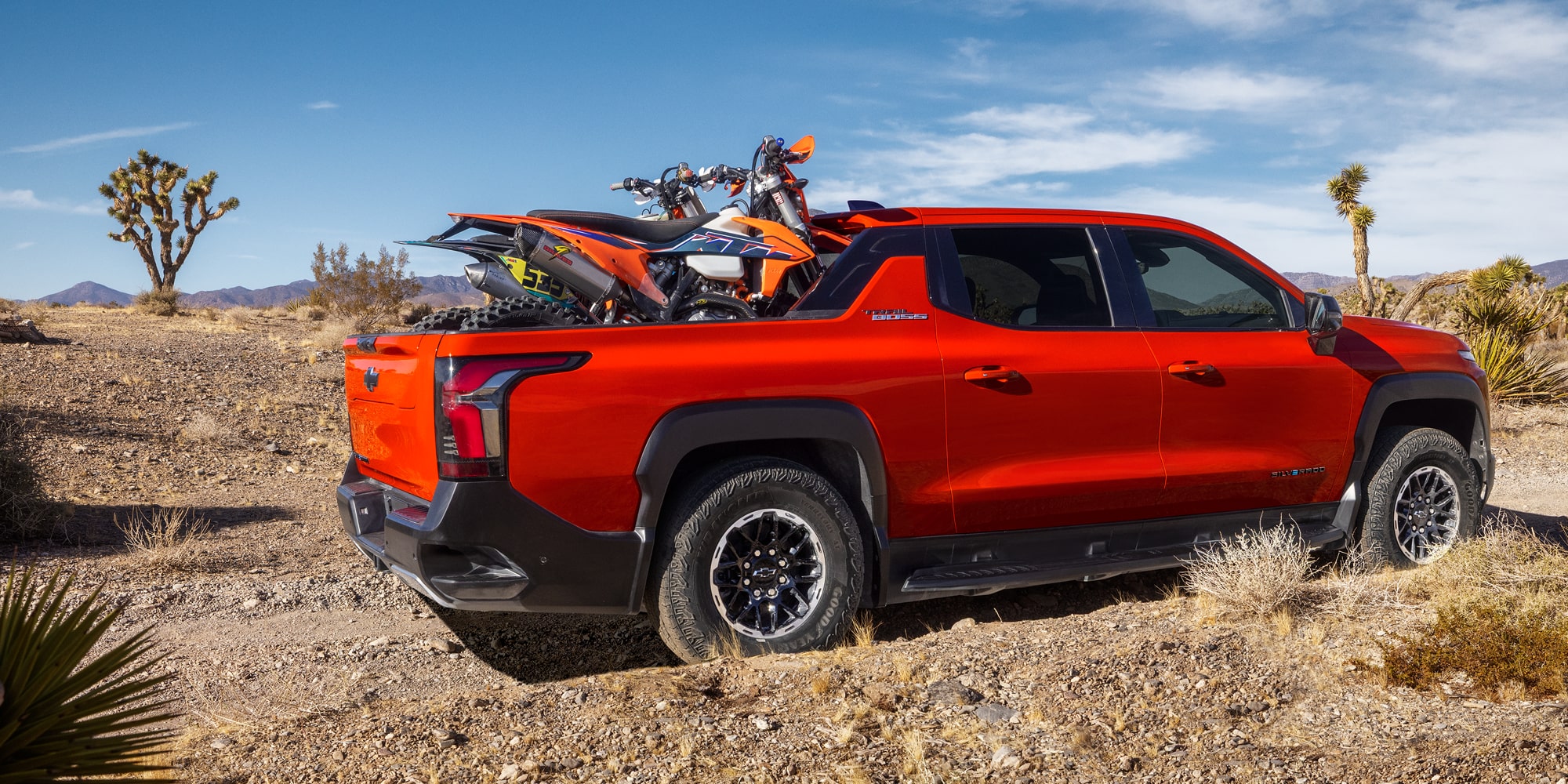 Three Quarters View of an Orange 2026 Chevy Silverado EV with a Dirt Bike on the Cargo Bed