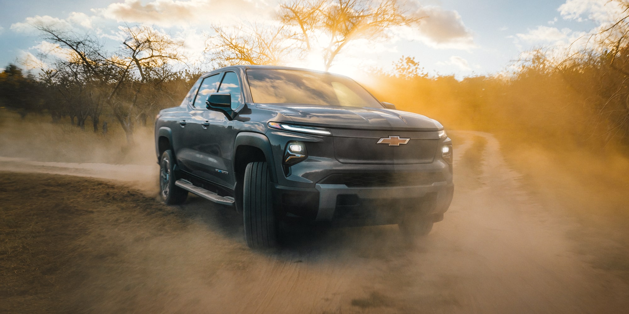 Three Quarters View of an Orange 2026 Chevy Silverado EV in a Rocky Plain near Mountains
