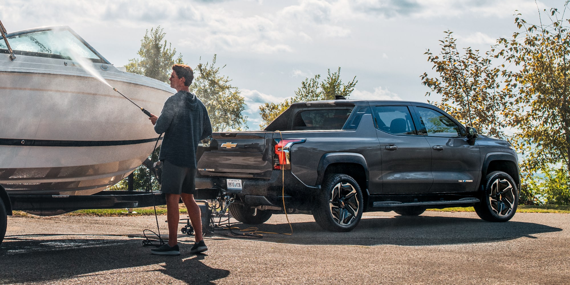 Three Quarters View of a 2027 Chevy Silverado EV Pulling Out a Speed Boat of the Shores of a Body of Water at Evening