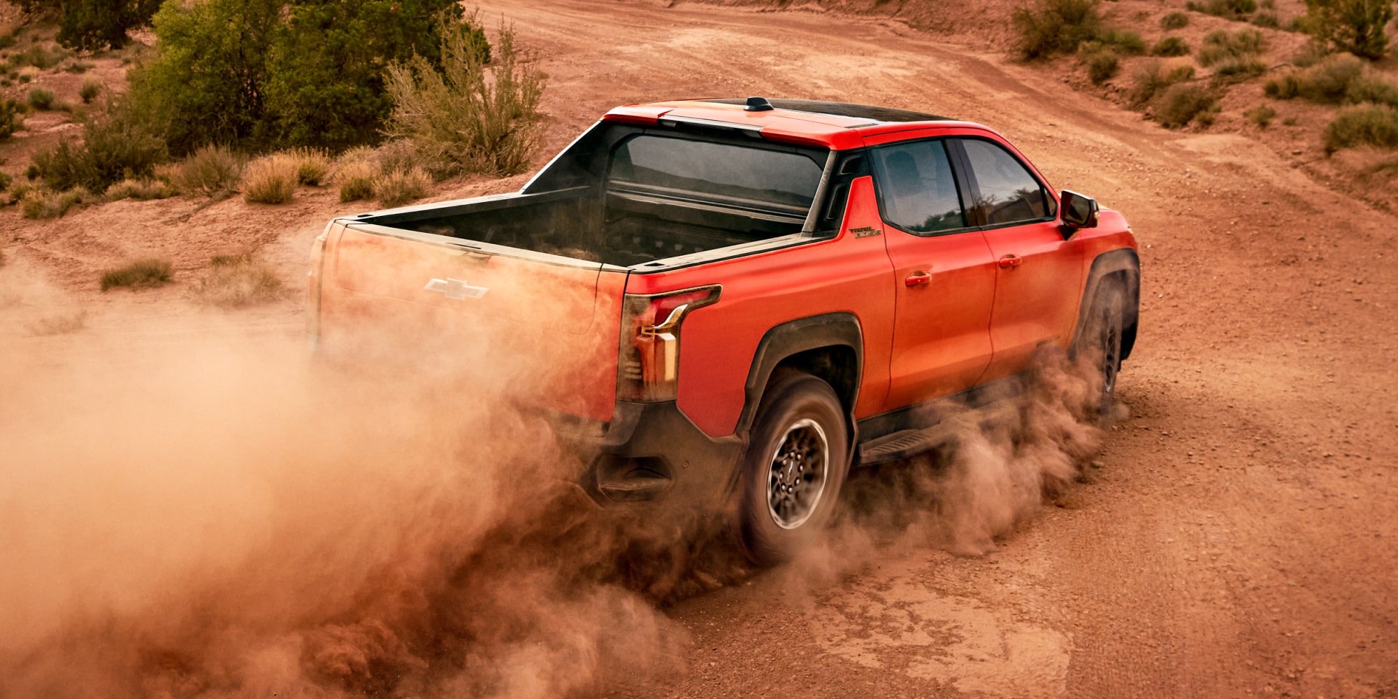 A Red Chevy Silverado EV Driving Through a Dusty Off-Road Trail.