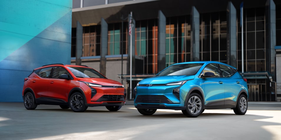 A Red and Blue 2027 Chevrolet Bolt Parked in Front of an Industrial Building and a Large Blue Wall