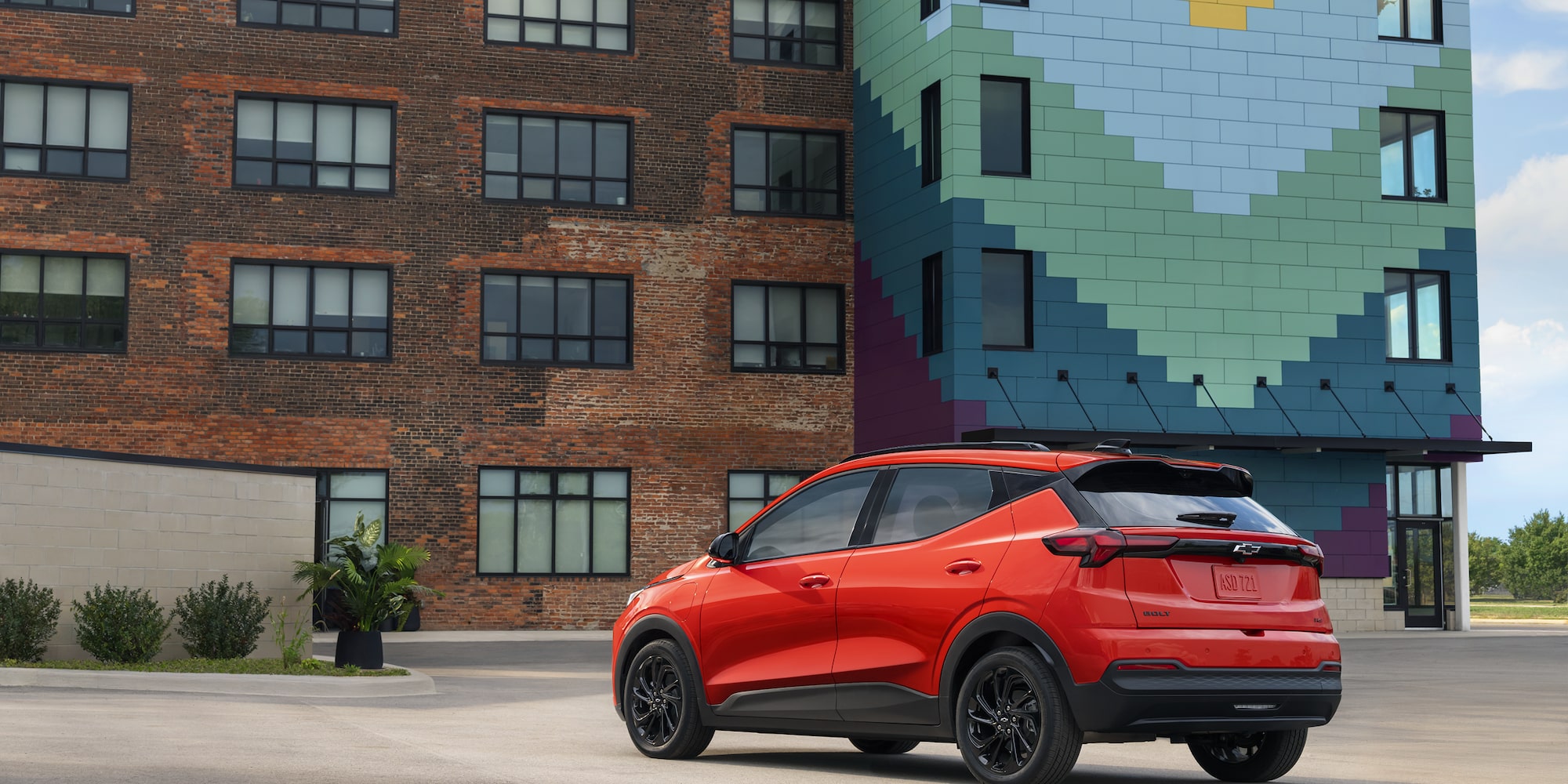 The Rear View of a Red 2027 Chevrolet Bolt Parked in Front of a Brick Building