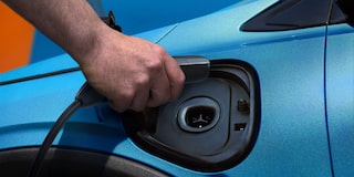 Close-up of a Hand Plugging in a Charging Cable into the Charging Port of a Blue 2027 Chevy Bolt