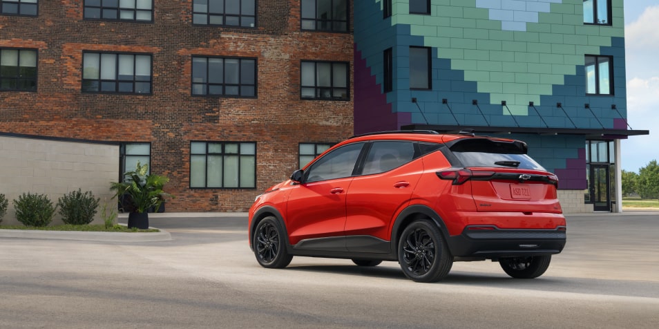 The Rear View of a Red 2027 Chevrolet Bolt Parked in Front of a Brick Building