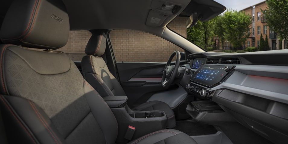 The Sun Shining into the Interior of a 2027 Chevrolet Bolt RS, Showing the Black Evotex Front Seat with Red Stitching and the RS Badge on the Headrest