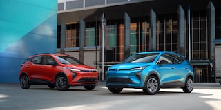 A Red and Blue 2027 Chevrolet Bolt Parked in Front of an Industrial Building and a Large Blue Wall