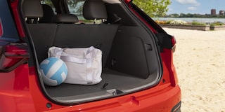 The Trunk of a Red 2027 Chevrolet Bolt is Open on a Sandy Beach, with a Blue and White Volleyball and a White Duffel Bag Inside