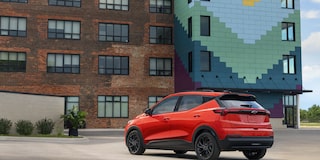 The Rear View of a Red 2027 Chevrolet Bolt Parked in Front of a Brick Building