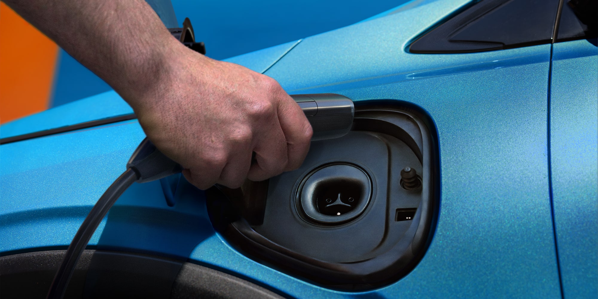 Close-up of a Hand Plugging in a Charging Cable into the Charging Port of a Blue 2027 Chevy Bolt