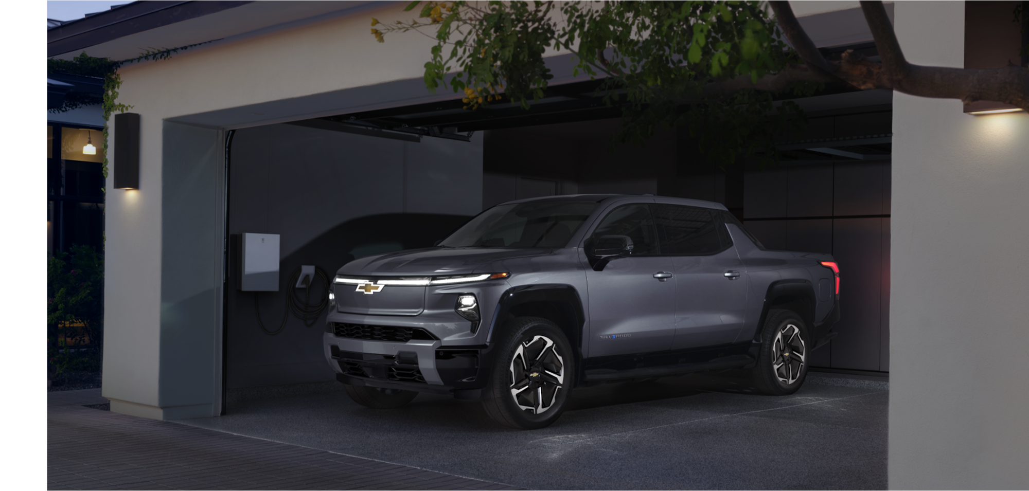 A Gray Chevrolet Silverado EV Parked in a Modern Garage and Connected to a Wall Charger.