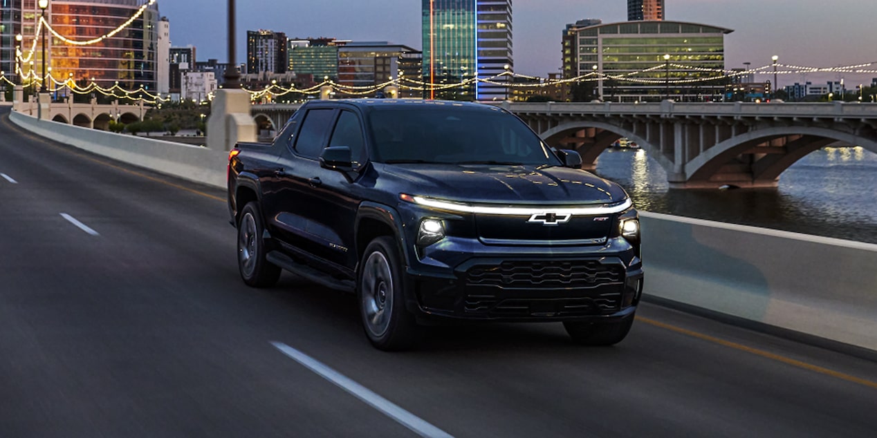 Black Silverado EV Driving on a Highway at Night with Cityscape in the Background