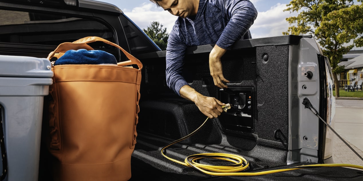 A Man Plugging an Extension Cable into the Outlets in the Bed of the Silverado EV