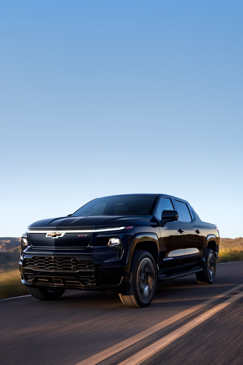 Black Silverado EV Driving Down a Scenic Highway at Dusk