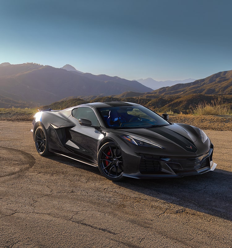 A Chevrolet Corvette Grand Sport X Is Parked on a Sunlit Road With Rolling Hills and Mountains in the Background at Golden Hour.