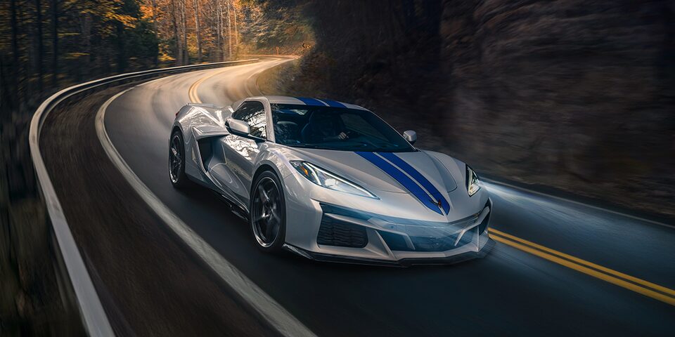 Evening shot of white Corvette E-Ray with blue band on the car driving through the forest