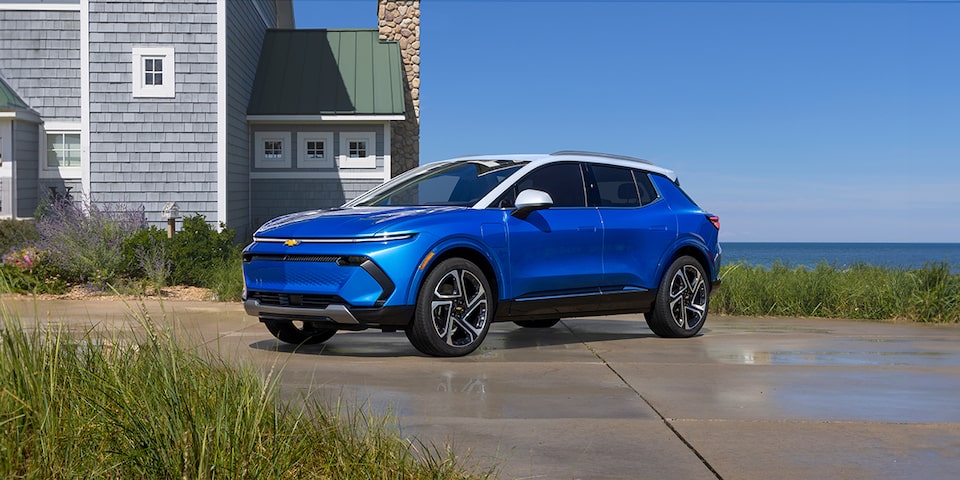 Toma matutina de una Equinox EV azul con techo blanco estacionada fuera de una casa