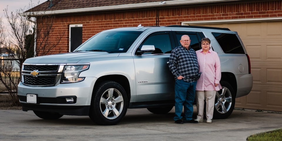 A Couple Stands Proudly Along Side Their Chevy Vehicle
