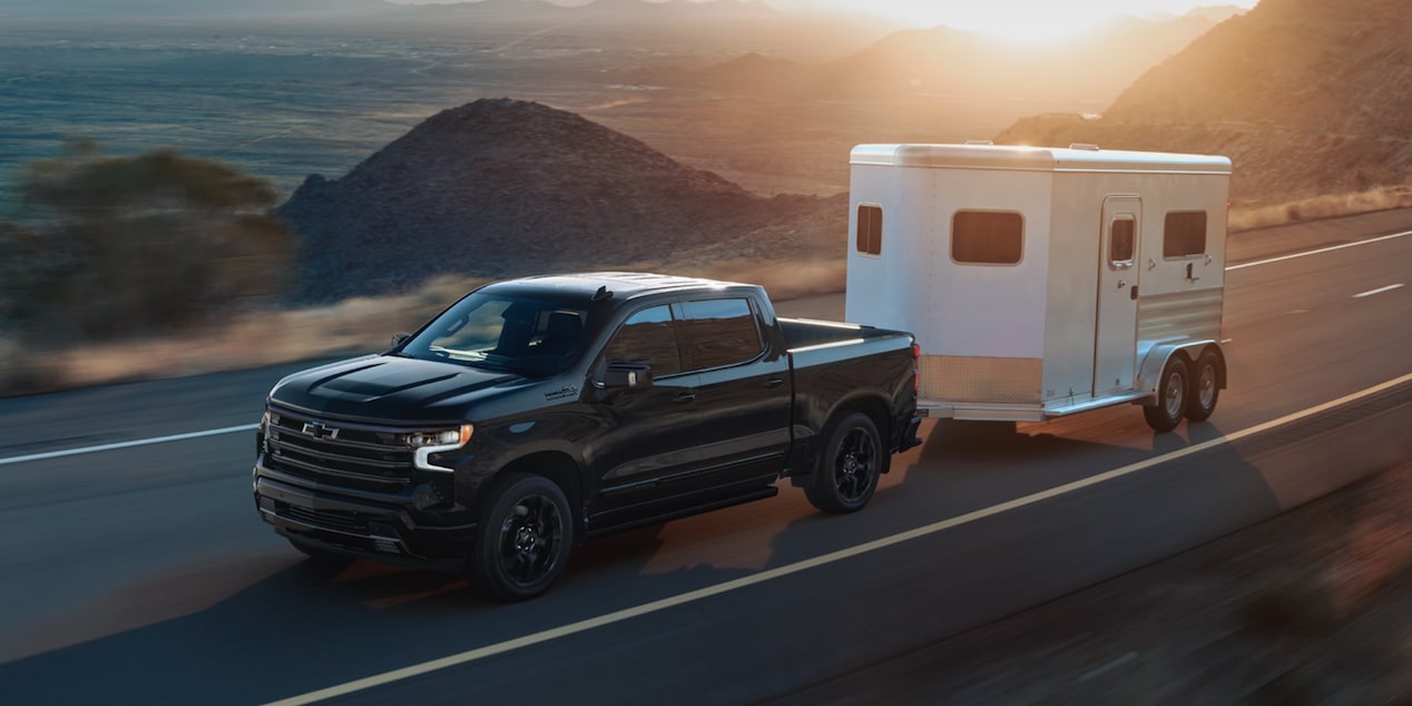 A Chevy Silverado Pulling a Horse Trailer Down a Mountain Road During Sunset