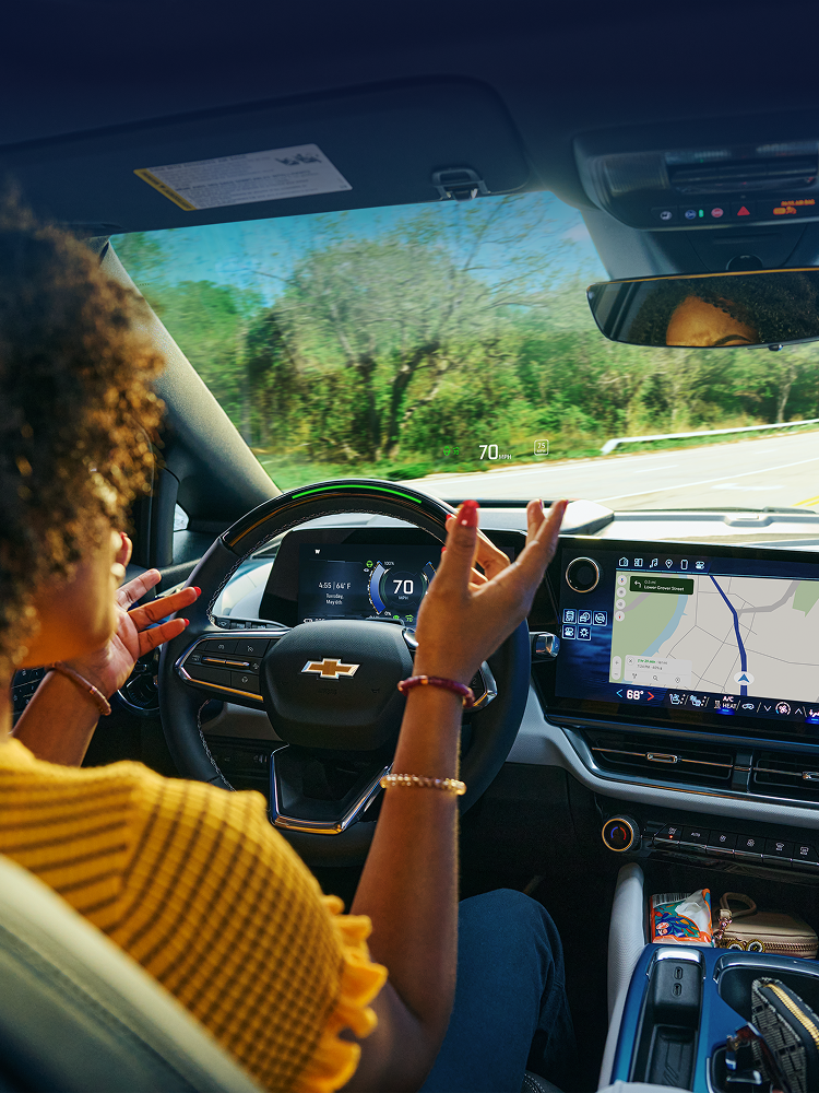 A Woman Talking Hands Free to a Passenger While Driving a Chevy Utilizing Super Cruise with Text Overlay Reading "Learn More About Super Cruise"