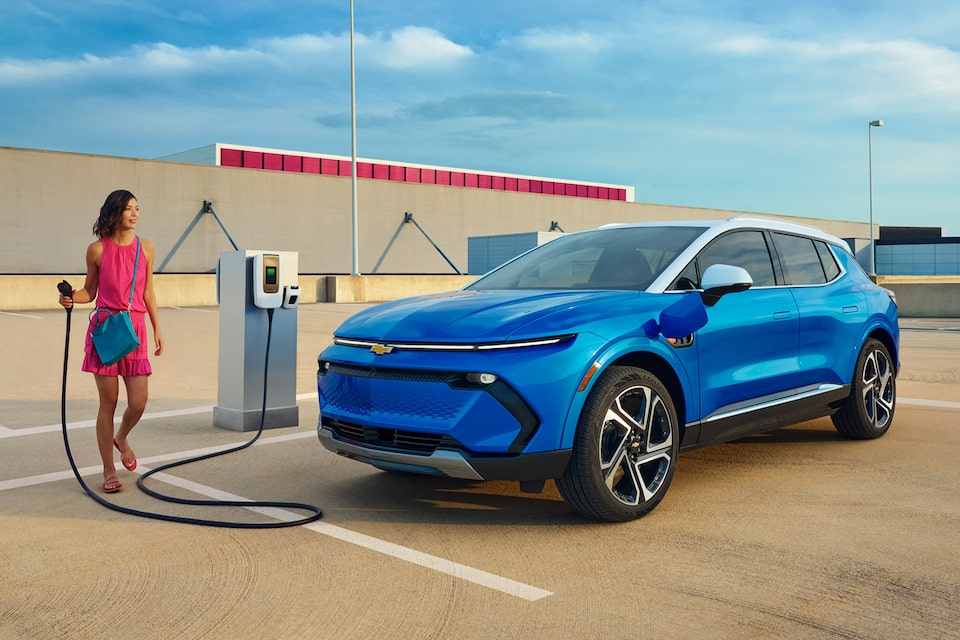Blue Equinox EV stationed outside charging station, with female model holding electric charger