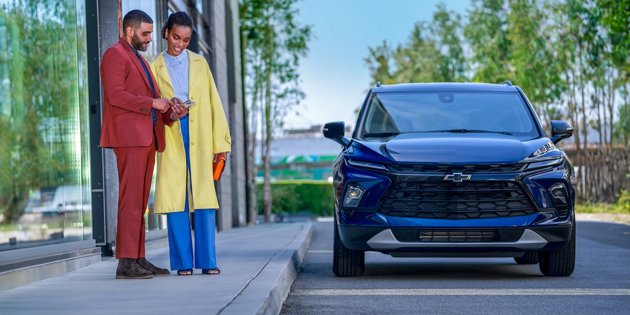 A Couple Looking at Their Phone While Standing on the Sidewalk Next to Their Chevy SUV