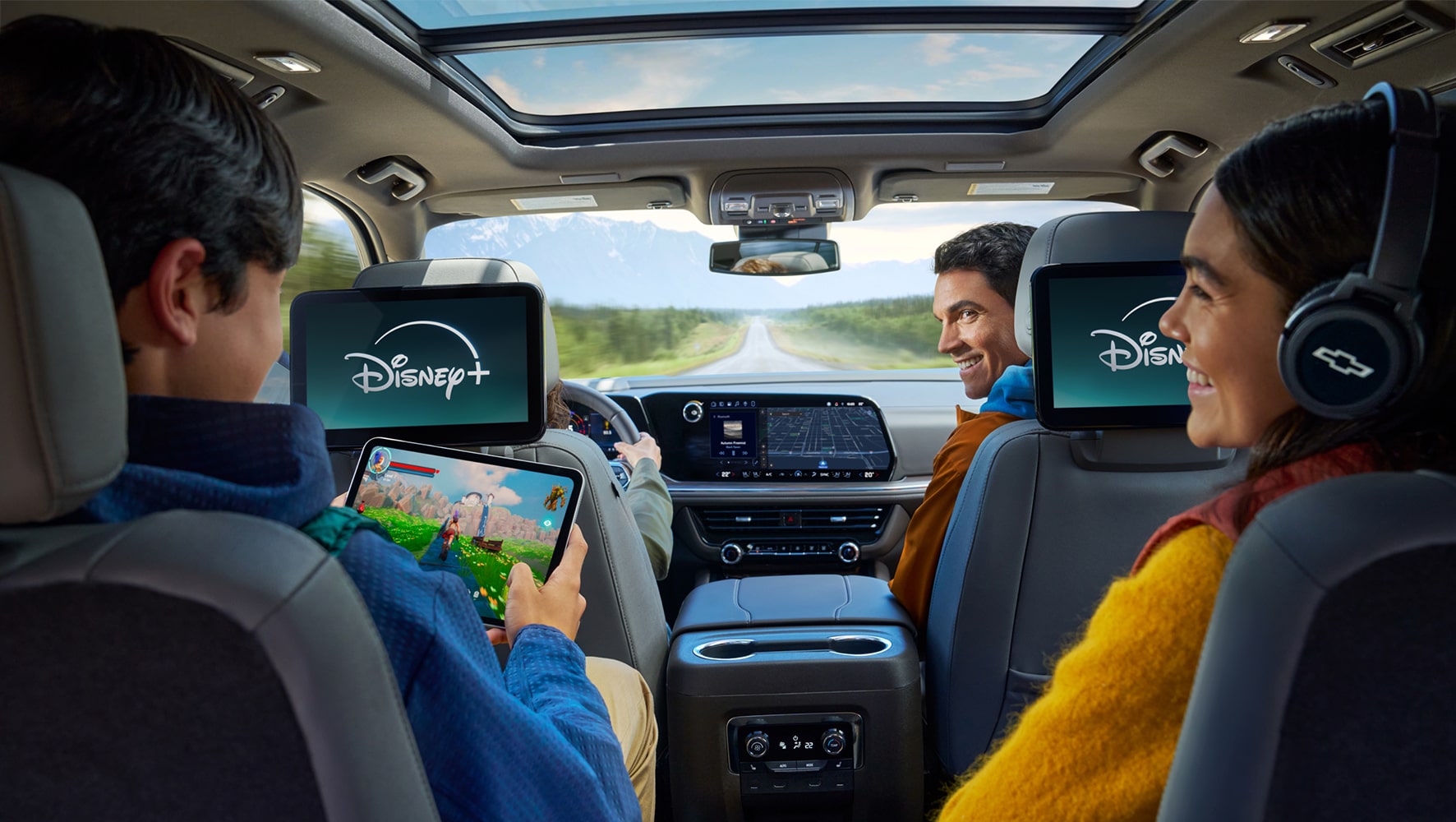 A family of four in a Chevy vehicle with a young boy holding a tablet in the backseat and the other passengers looking at him and smiling.
