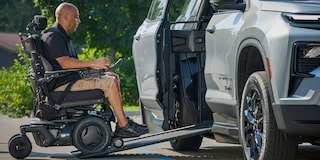 A Person in a Motorized Wheelchair Using an Extended Wheelchair Ramp to Enter a Silver Chevy Traverse SUV Parked Outdoors.