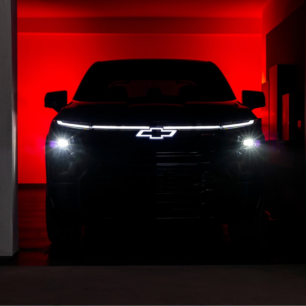 Chevy Silverado EV Parked in a Dark Garage with Headlights and Logo Illuminated