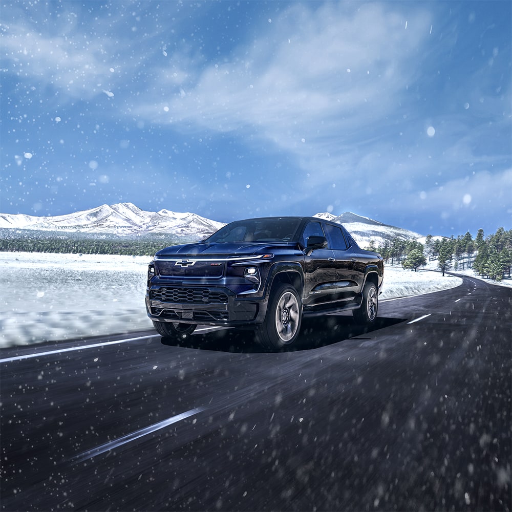 Un vehículo Chevy Silverado EV andando por una carretera con montañas nevadas de fondo