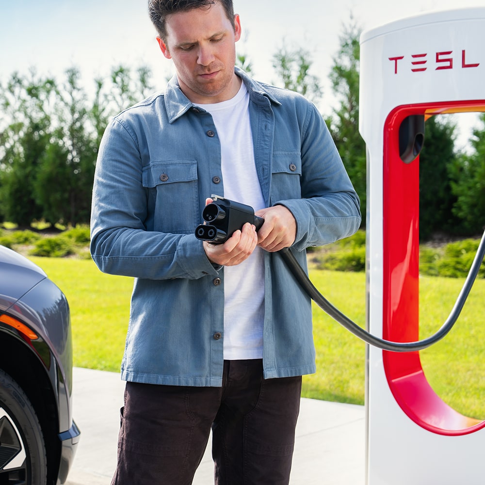 Un hombre usa un cargador público para EV de Tesla para cargar su Chevy EV