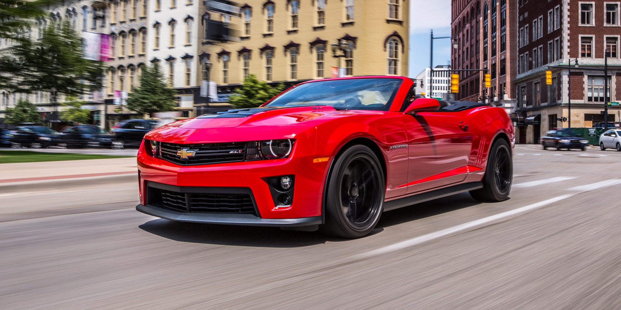 Red Convertible Chevy Sports Car Driving through a City Street with Brick Buildings in the Background