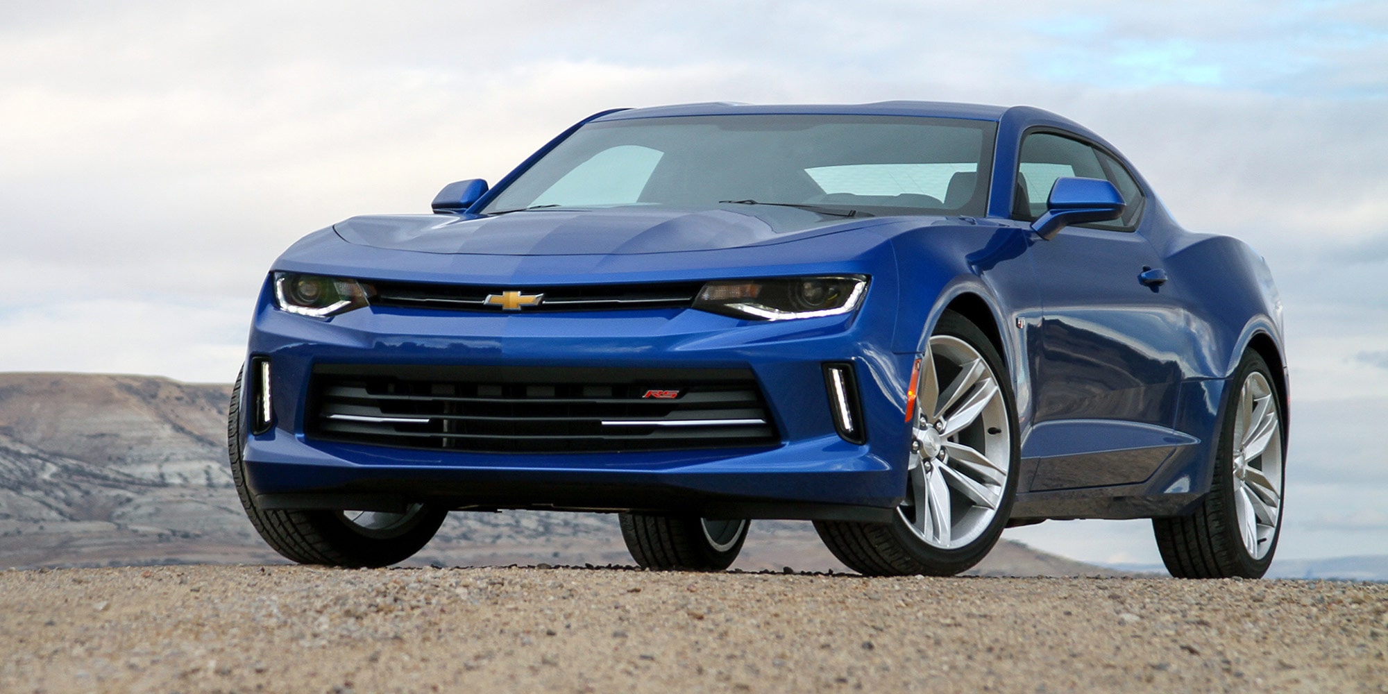 Blue Modern Chevy Sports Car Parked on an Open Land with Mountains in the Background