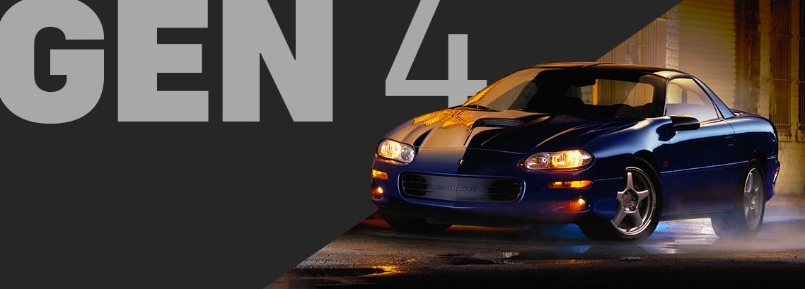 Dark Blue Chevy Camaro at Night with Headlights On, Parked with Warm Yellow Light Reflecting off the Wet Pavement