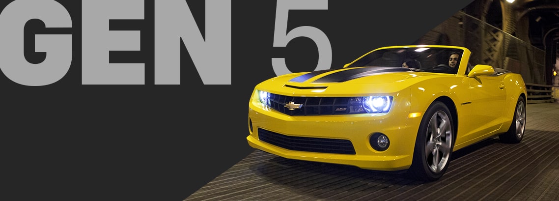 Front Angle View of a Bright Yellow Chevy Camaro Convertible Driving at Night with Its Headlights Glowing