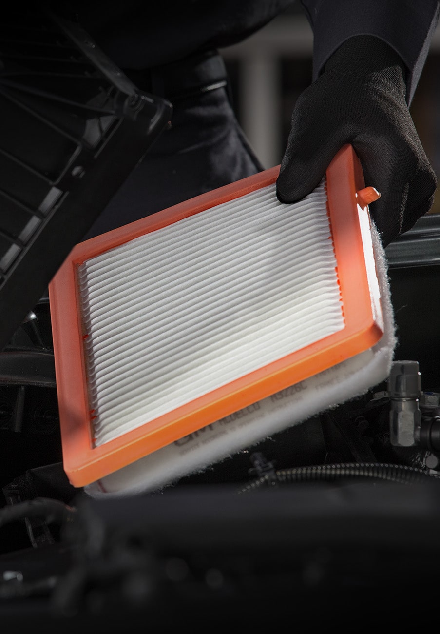 Gloved Technician Holding a Rectangular Orange-Framed Engine Air Filter under an Open Hood