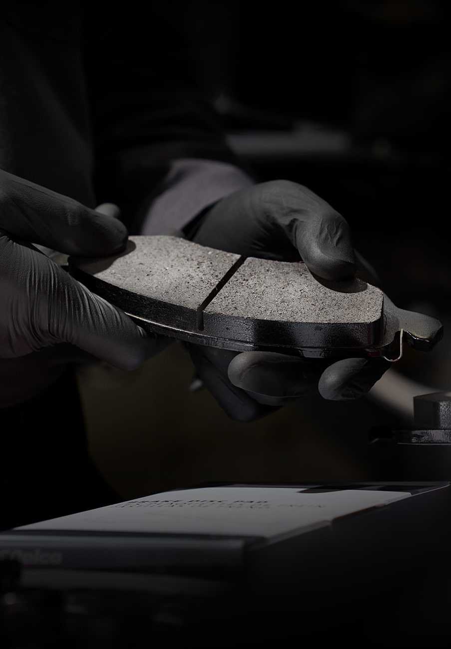 Mechanic Wearing Gloves Holding a Pair of New Brake Pads under a Spotlight