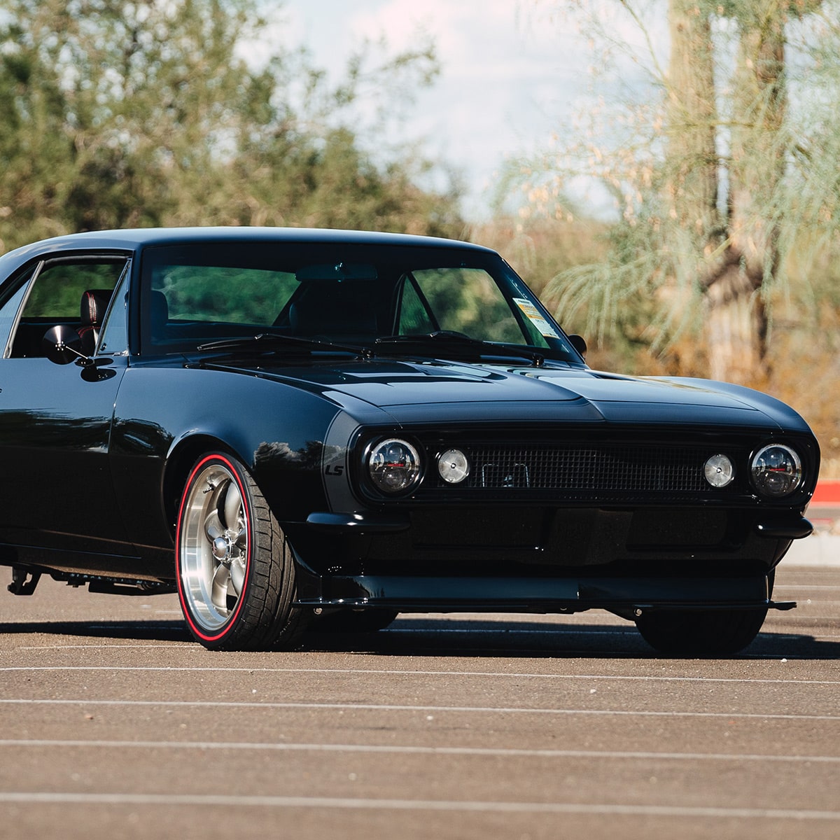 Three Quarter View of a Black Classic Chevy Camaro Parked on a Road with Some Trees in the Background