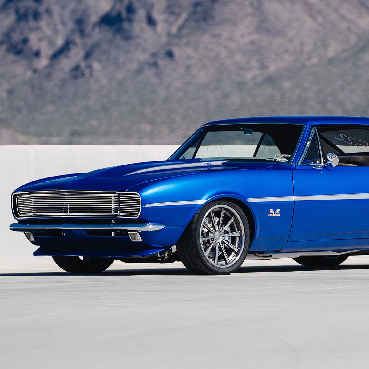 Bright Blue Classic Chevy Camaro Parked on an Open Concrete Surface with Mountains in the Background