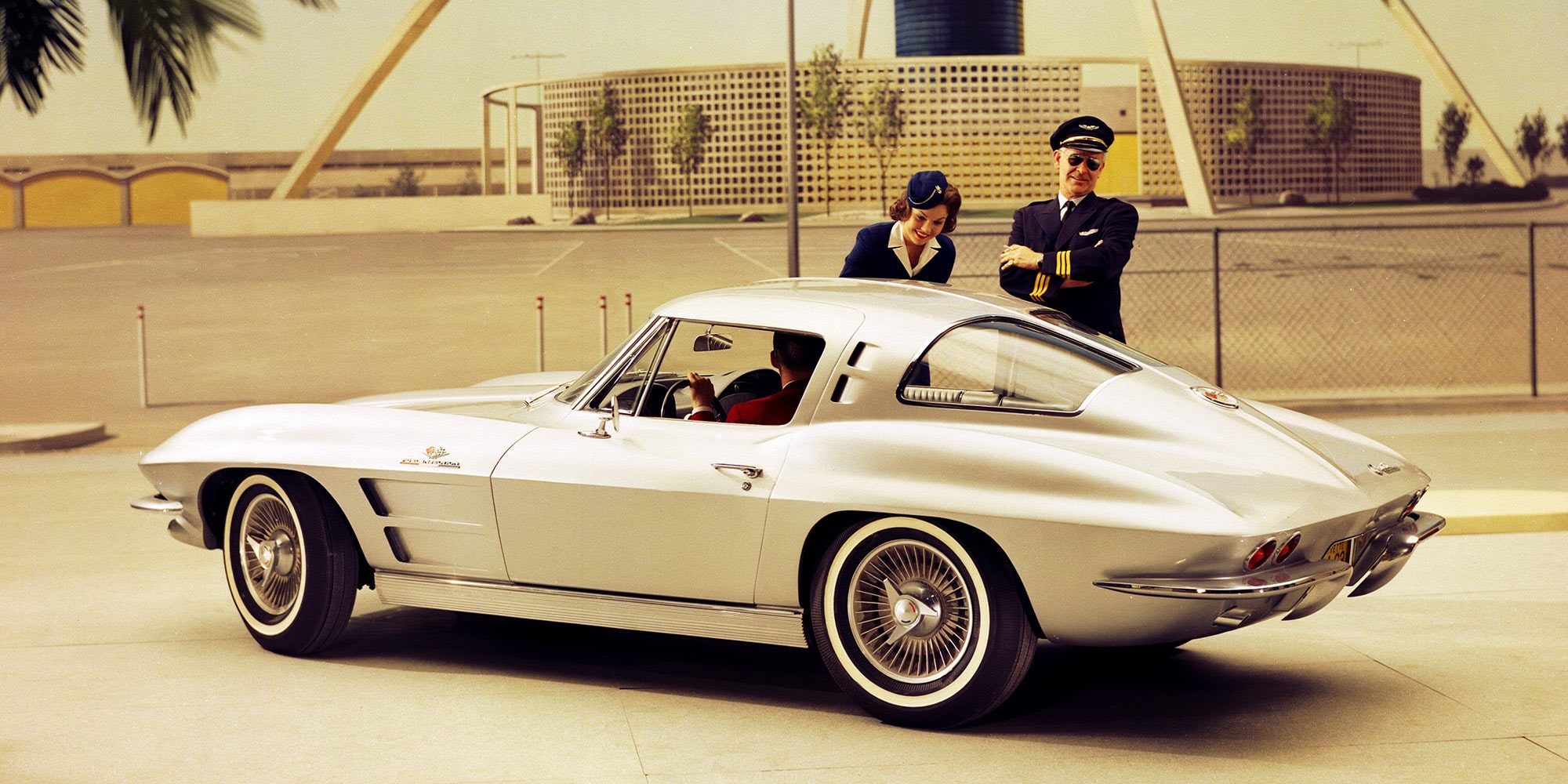A White Classic Chevrolet Corvette Convertible with Blue Racing Stripes Parked Outdoors.