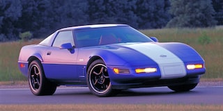 A Blue Chevrolet Corvette with White Racing Stripes Driving on a Road.