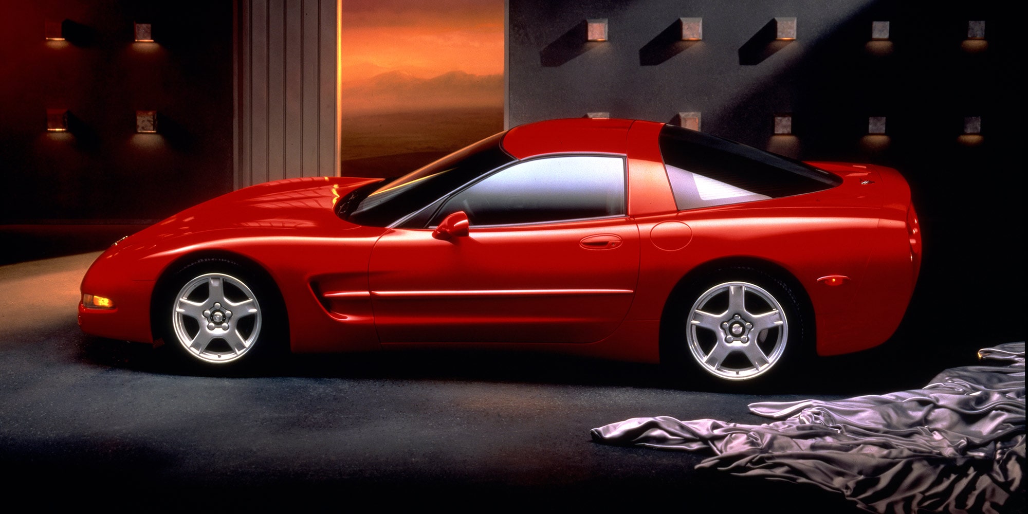 A Red Chevrolet Corvette Displayed Indoors Under Warm Lighting with Chrome Wheels.